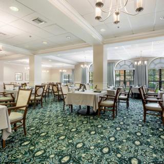 An elegant dining room featuring neatly arranged tables and chairs, with decorative chandeliers and a patterned carpet.