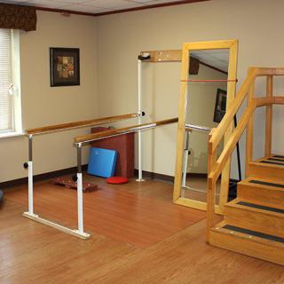 A rehabilitation therapy room with balance bars, a mirror, and stairs for physical exercises.