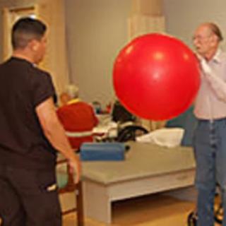 A person engages in physical therapy using a large red exercise ball under the guidance of a therapist.