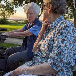 Two elderly women enjoying a conversation in the park during sunset.