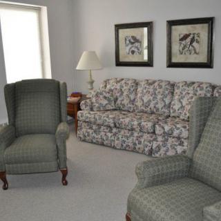 A cozy living room with a floral sofa, two plaid armchairs, and decorative artwork on the wall.