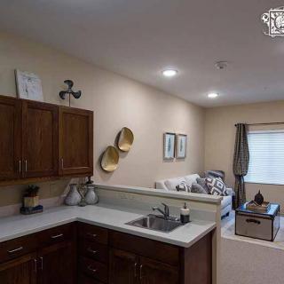 An open-concept kitchen with dark wood cabinets and a view into a cozy living room area.