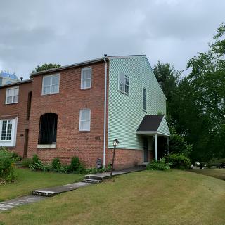 A two-story brick and siding house with a front lawn and surrounding trees under a cloudy sky.