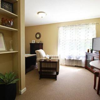 A cozy living room with an armchair, television, and a bookshelf by the window.