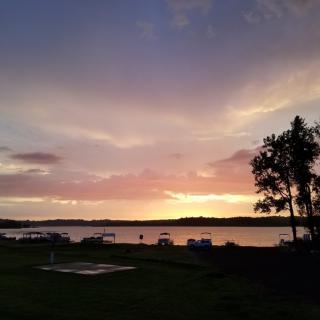 A serene sunset over a tranquil lake with silhouetted trees and colorful clouds.