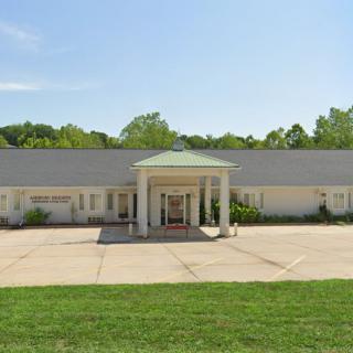 A single-story building with a central entrance, surrounded by greenery and under a clear sky.