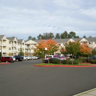 A residential apartment complex with a parking lot and colorful autumn trees under a cloudy sky.