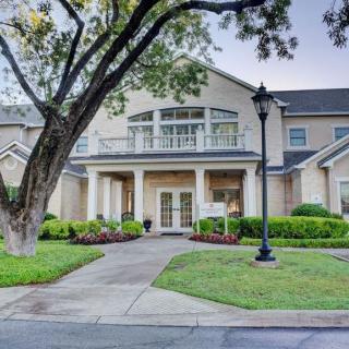 A large, elegant residential building with a well-maintained lawn and trees, featuring a central pathway and lamp post.