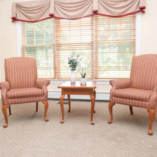 A cozy living room setup featuring two armchairs and a small table in front of a window with blinds and curtains.