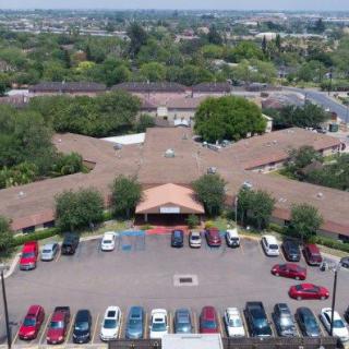 Aerial view of a building with a parking lot filled with cars, surrounded by trees in a suburban area.
