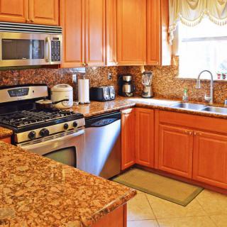 A well-lit kitchen with wooden cabinets, stone countertops, and modern appliances including a stove and microwave.