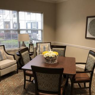 A cozy dining area with a wooden table, surrounding chairs, a lamp by the window, and artwork on the wall.