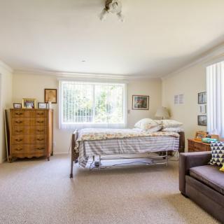 A cozy bedroom with a bed, dresser, and large windows allowing natural light.
