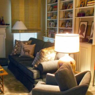 A cozy living room with a sofa, lamp, and bookshelves filled with decor items.