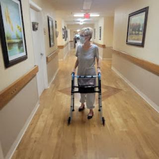 An elderly person using a walker in a healthcare facility corridor.