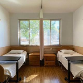 A minimalist hospital room featuring two beds, a window, and a privacy curtain.