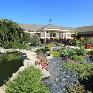 A beautifully landscaped garden with a pond and pathway leading to a building under a clear blue sky.