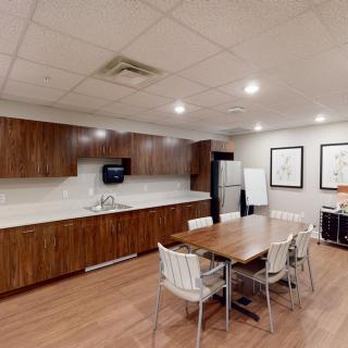A modern office kitchen and break room with wooden cabinets, a central table, and various appliances.