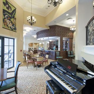 A stylish lounge area featuring a grand piano, elegant chandeliers, and arranged dining tables, creating a cozy and inviting atmosphere.