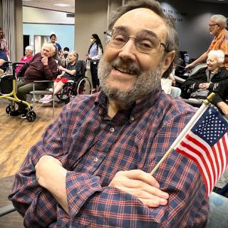 A cheerful man holding an American flag at a community gathering.