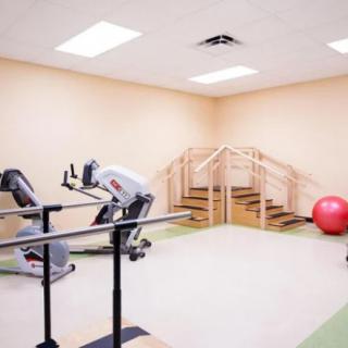 A clean and bright physical therapy room equipped with exercise machines, a medicine ball, and a staircase setup.