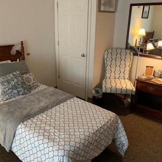 A cozy bedroom with a single bed, a patterned chair, and a mirror on the dresser.