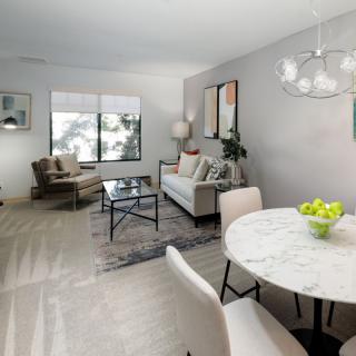 A modern living room with minimalist decor featuring a sofa, armchairs, and a dining table in light neutral tones.