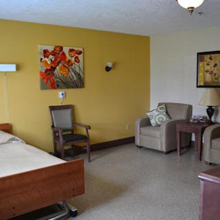 A well-furnished hospital room featuring a bed, comfortable chairs, and decorative artwork on the walls.