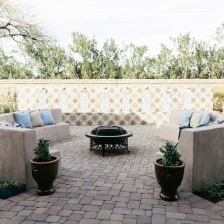 A cozy patio with comfortable seating around a fire pit, adorned with potted plants and enclosed by a decorative wall.