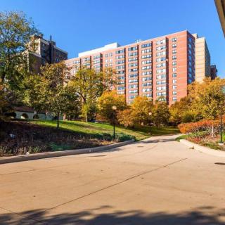 A tall apartment building surrounded by autumn trees and a pathway in an urban setting.