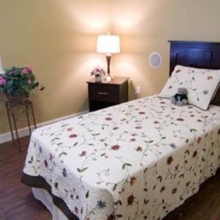 A cozy bedroom with a single bed adorned with a floral quilt, a nightstand featuring a lamp and decor.