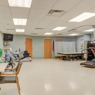 A spacious rehabilitation room equipped with various exercise machines and therapy tables.