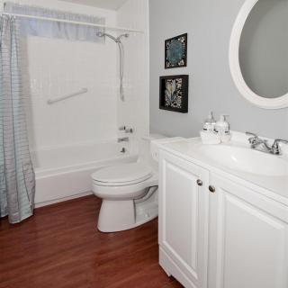 Modern bathroom with white fixtures and hardwood flooring.