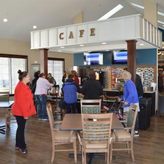 A group of people gathered in a cafe, standing near the counter with tables and chairs around.