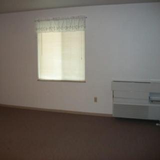 A minimalist empty room with a window, carpet flooring, and an air conditioning unit.