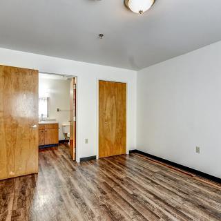 An empty room with hardwood flooring, white walls, and wooden doors leading to another room.