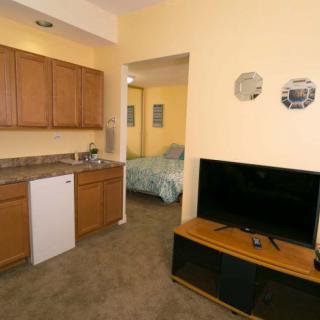 Cozy apartment living area with kitchen and TV setup, leading into a bedroom.