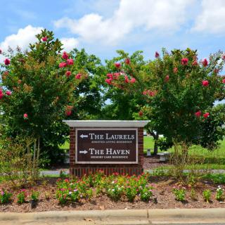 A directional sign surrounded by trees and flowers on a sunny day.