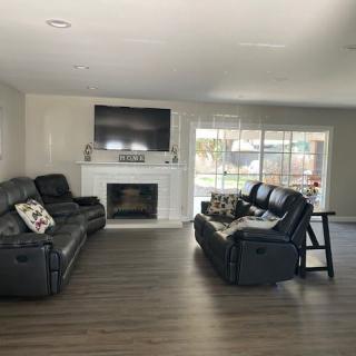 A modern living room with black sofas, a television above a fireplace, and hardwood flooring.