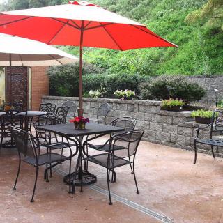 A pleasant outdoor patio with tables, chairs, and red umbrellas surrounded by greenery.