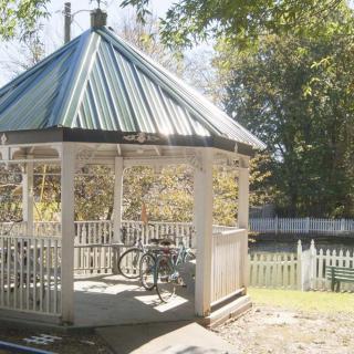 A quaint gazebo surrounded by trees and bathed in autumn sunlight.