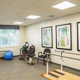 A rehabilitation room equipped with exercise machines, an exercise ball, and parallel bars.
