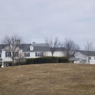 A spacious residential house set against a cloudy sky, surrounded by bare trees and dry grass.