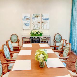 A well-arranged dining room with a wooden table, cushioned chairs, floral centerpiece, and decorative wall art.
