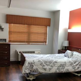 A tidy hospital room with a single bed, wooden blinds, and warm lighting.