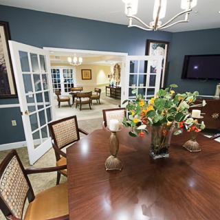 Elegant dining room with a wooden table and floral centerpiece, leading to an adjacent room through open French doors.