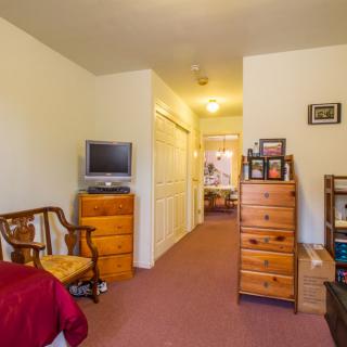 A cozy bedroom with wooden furniture, a TV, and a view into a hallway.