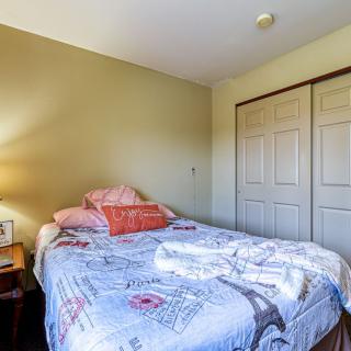 A cozy bedroom featuring a neatly made bed with patterned linens, a nightstand with a lamp, and a closed closet.