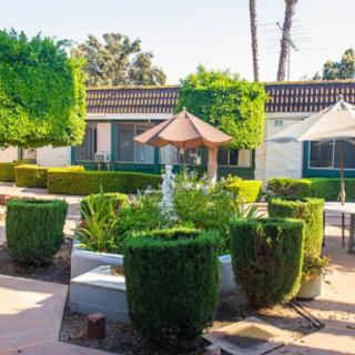 A well-maintained garden with a central fountain surrounded by trimmed hedges and patio umbrellas.