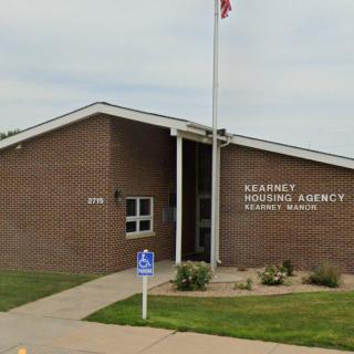 A brick building housing the Kearney Housing Agency with a flagpole and accessible parking.